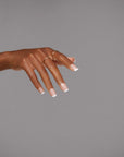 A poised hand featuring elegant French tip square nails with gold rings for a sophisticated look.