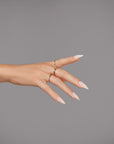 A beautifully posed hand featuring white almond-shaped nails adorned with gold rings.