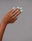 A stylish hand showcasing mint square nails complemented by a blue gemstone butterfly ring.