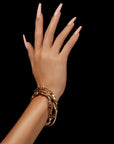 A hand adorned with long nude coffin nails against a black background, styled with gold bracelets.