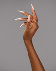 Stylish nude coffin nails showcased on an elegantly posed hand with gold jewelry against a neutral background.