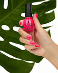 A lady's hand holding cutex bottle showing her nail color with leaf behind