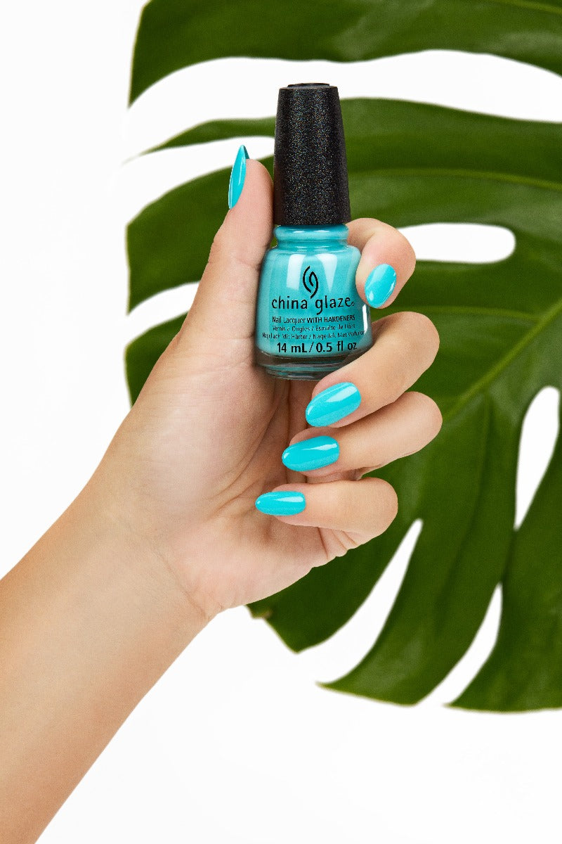 A woman's hand holding a creamy neon blue nail enamel with a leaf background