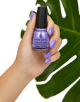 A lady's hand holding nail enamel showing her nail color with leaf behind