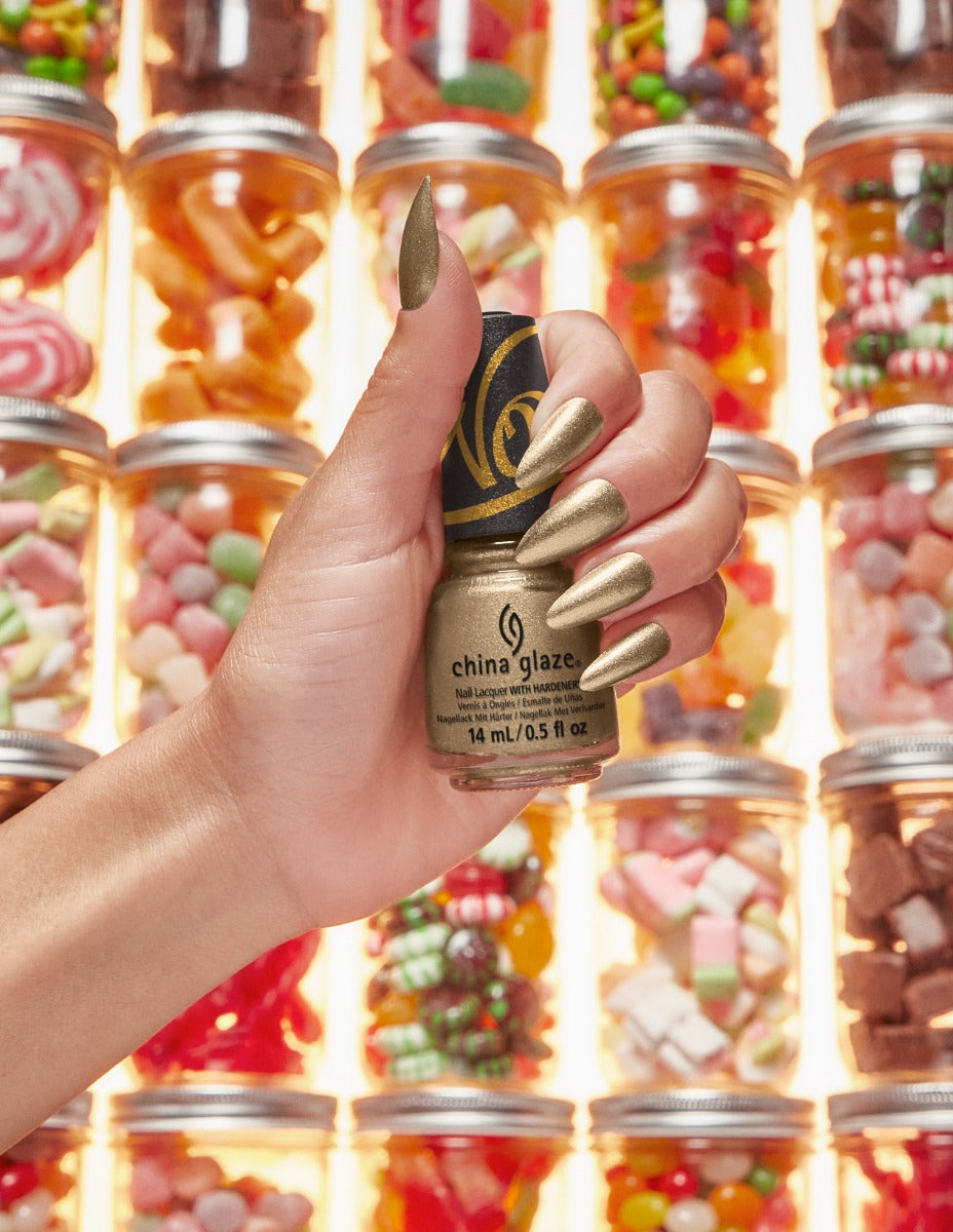 China Glaze golden nail polish held against a colorful candy jar background, reflecting a sweet, festive look.