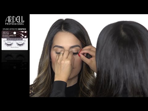 A professional makeup artist applying Ardell Studio Effects Wispies false eyelashes to a model for a voluminous lash look.