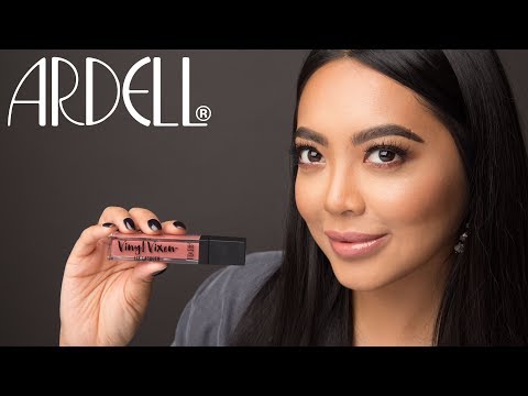 Model holding Ardell Vinyl Vixen lip lacquer, wearing bold lashes and glossy nude lipstick.