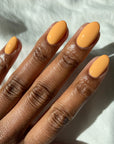 A lady's dark skin tone fingernails with painted almond shaped nails with Tangerine Heat creamy orange nail color