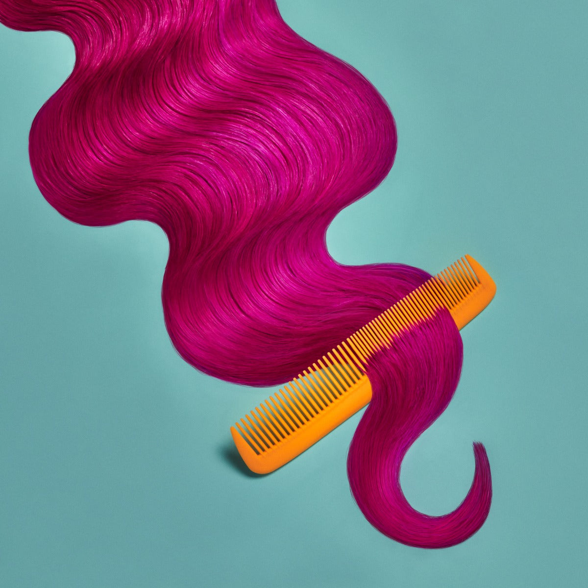 A section of wavy, bright pinkish-red hair on a teal background being combed at the end, showcasing the Punky Colour Sugar Cloud Semi Permanent Foam Color