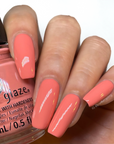 A Medium skin tone woman's hand nail with a glimpse of pink corally crème nail polish bottle from China Glaze