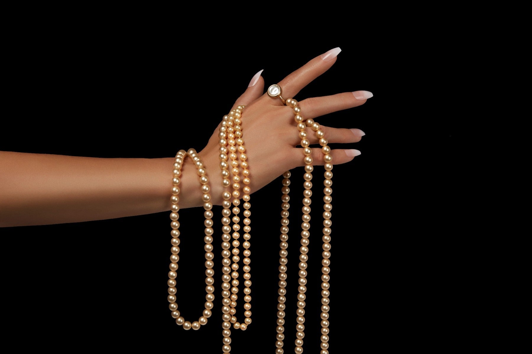 Hand wrapped in strands of gold pearls, showcasing French Fade press-on nails for an elegant and luxurious style.