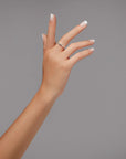 Stylish hand with natural-looking French tip nails, wearing a minimalist ring against a neutral gray background.