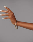 Hand with glossy French tip nails and gold bracelet, elegantly posed against a gray backdrop.