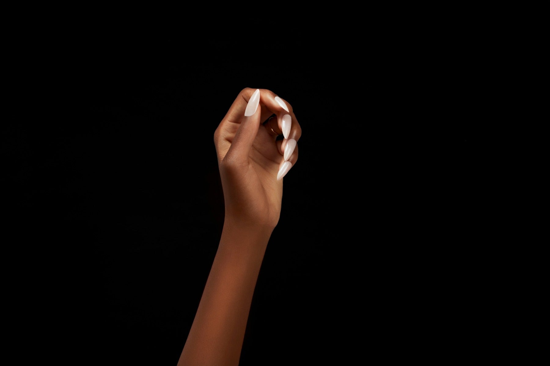 A hand elegantly posed with glossy white almond-shaped nails against a sleek black background.