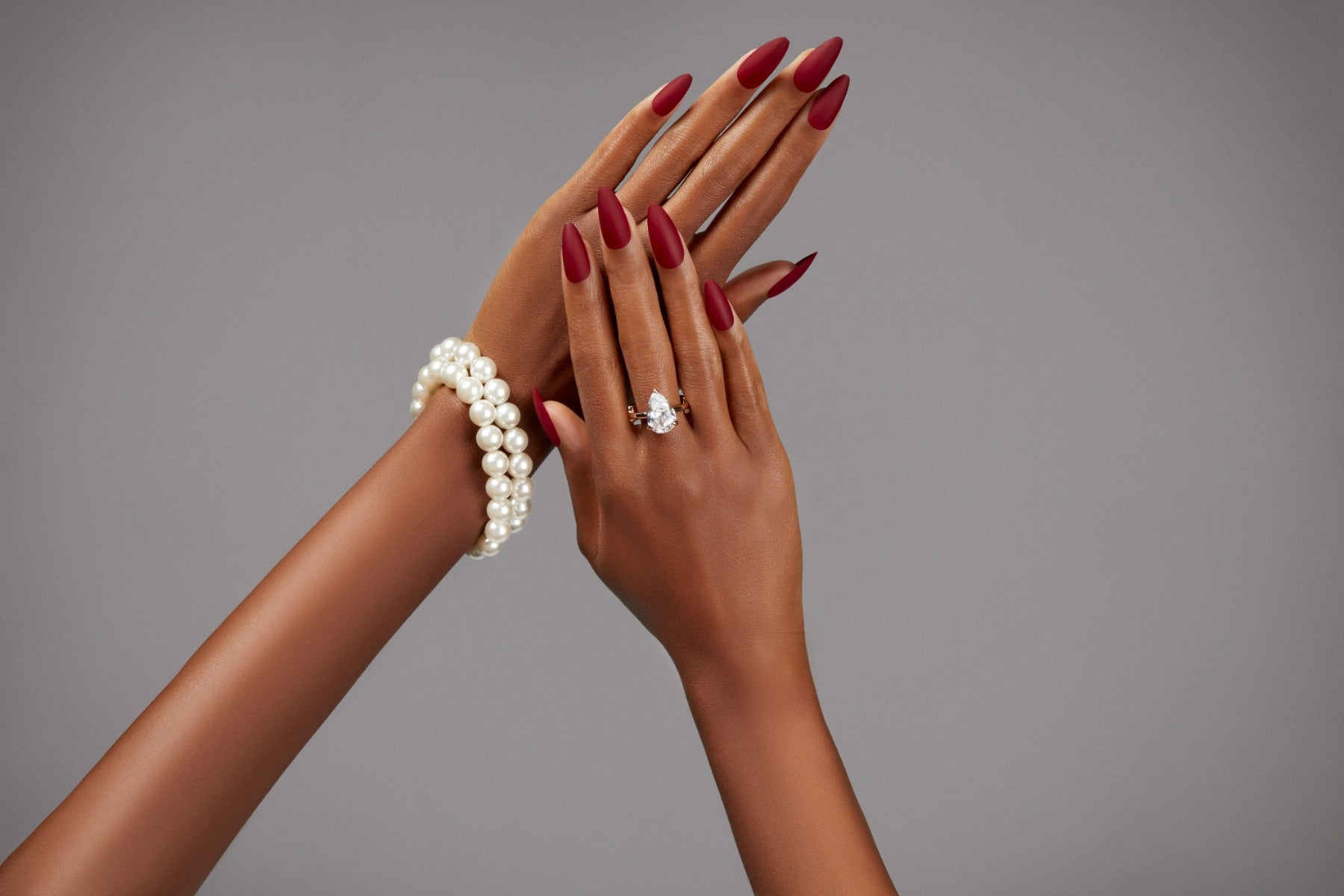 Classy hands adorned with Bordeaux nails, pearl bracelet, and a teardrop diamond ring.