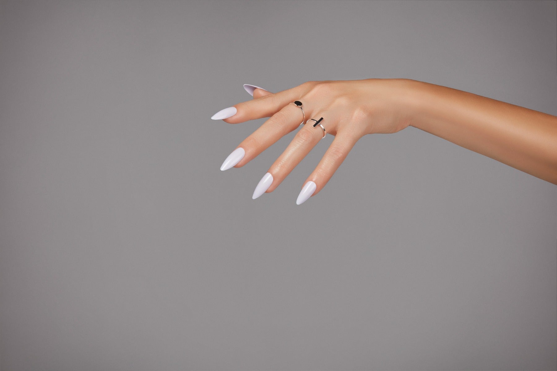Hand with lilac almond-shaped nails, accessorized with rings, against a neutral background for a soft, feminine look.
