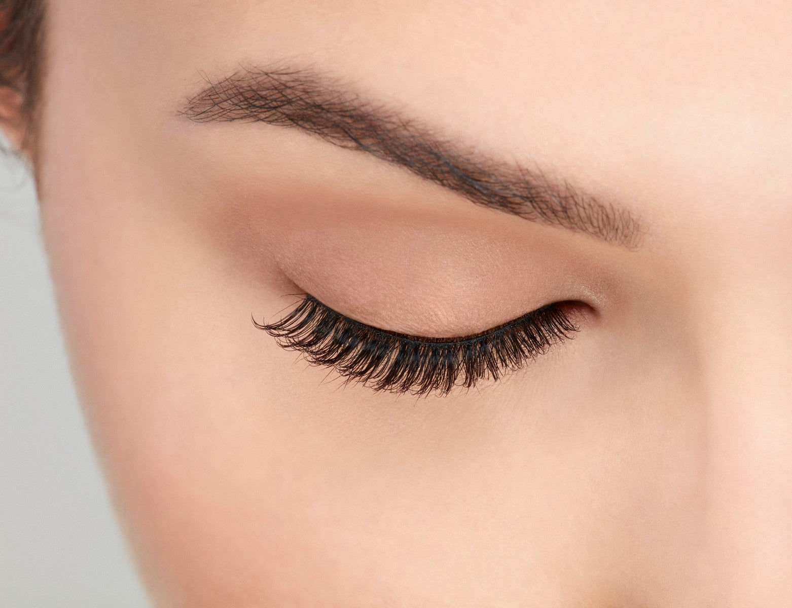 Angled close-up of a model's closed right eye wearing an Ardell Natural 174 lashes