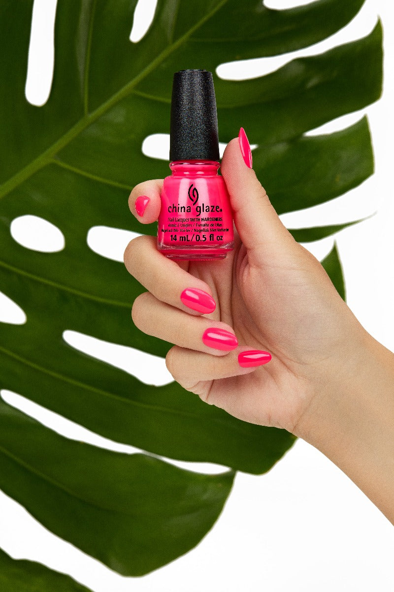A lady's hand holding cutex bottle showing her nail color with leaf behind