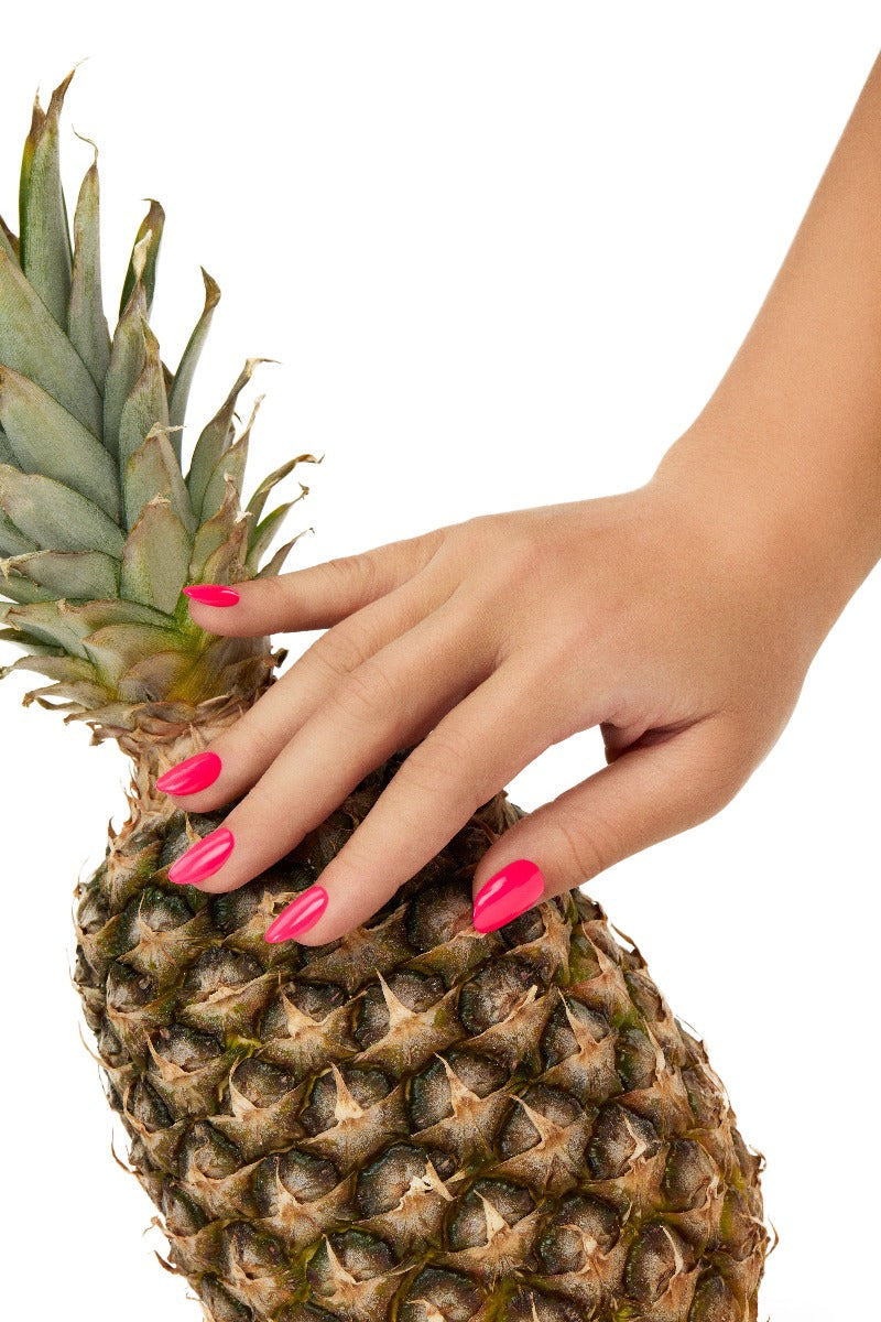 A woman touching a pineapple revealing her almond shape colored nails