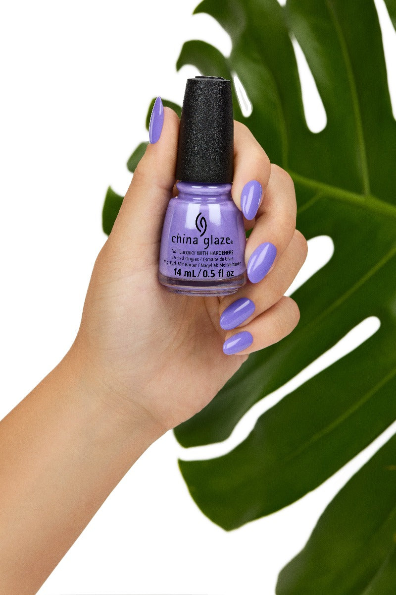 A lady's hand holding nail enamel showing her nail color with leaf behind