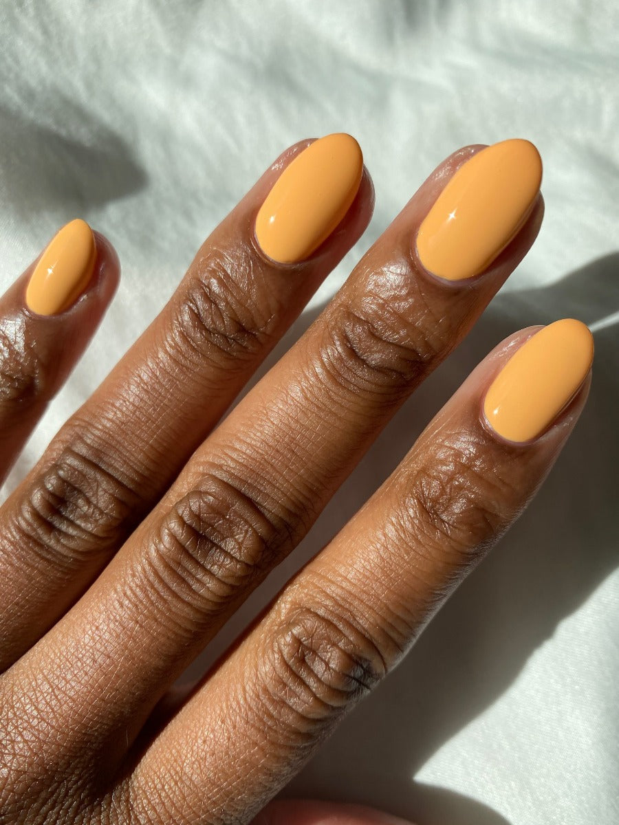 A lady's dark skin tone  fingernails with painted almond shaped nails with Tangerine Heat creamy orange nail color