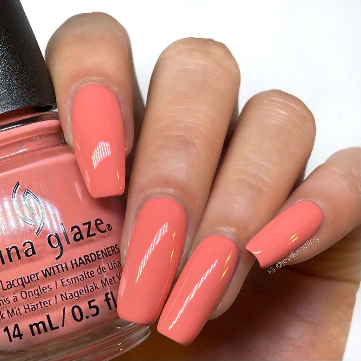 A Medium skin tone woman's hand nail with a glimpse of pink corally crème nail polish bottle from China Glaze